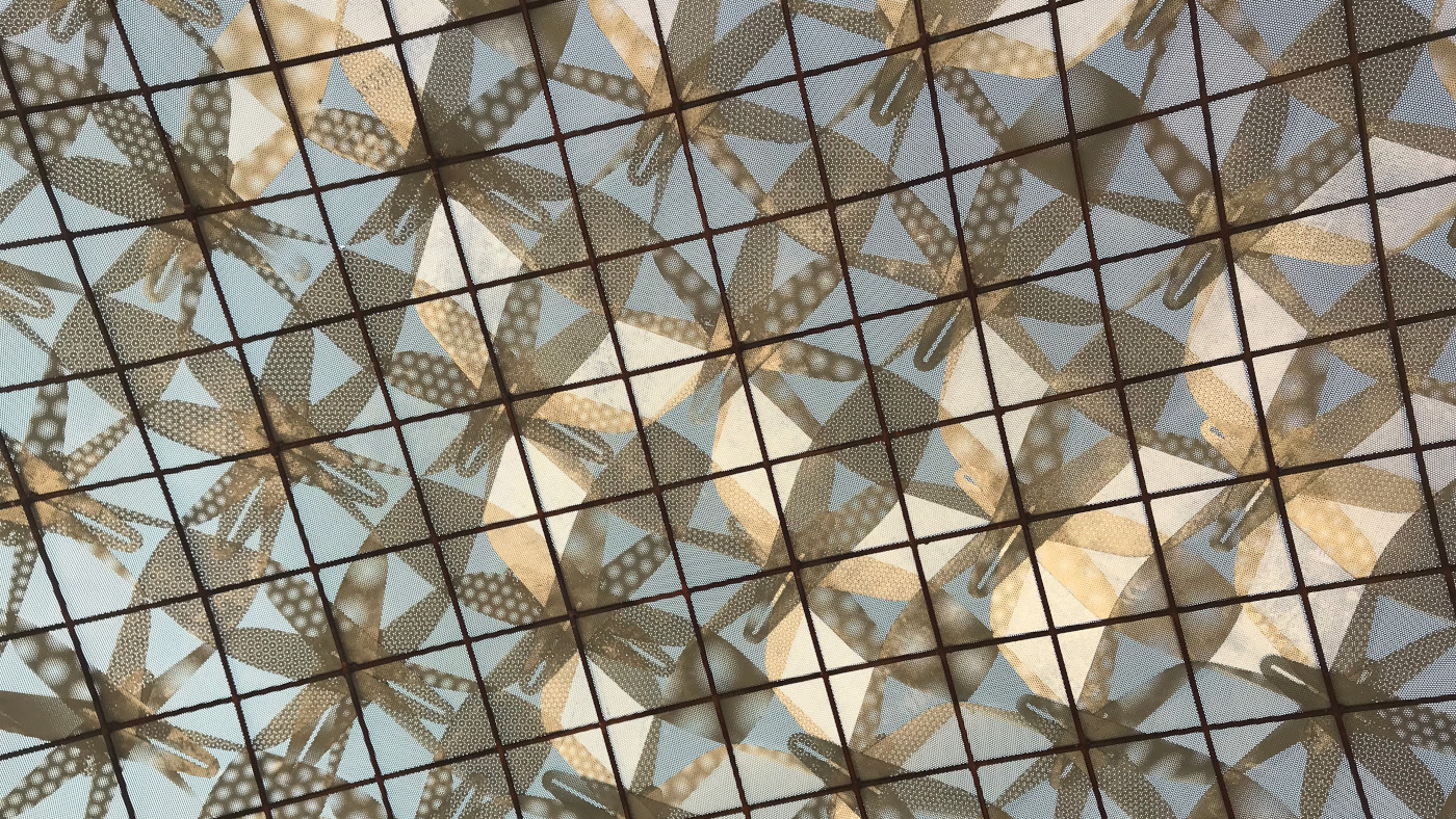 picture of a metal canopy with a grid of repeating patterns backlight by the sky